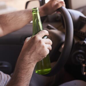bottle of beer in a man s hands driving the car during daytime