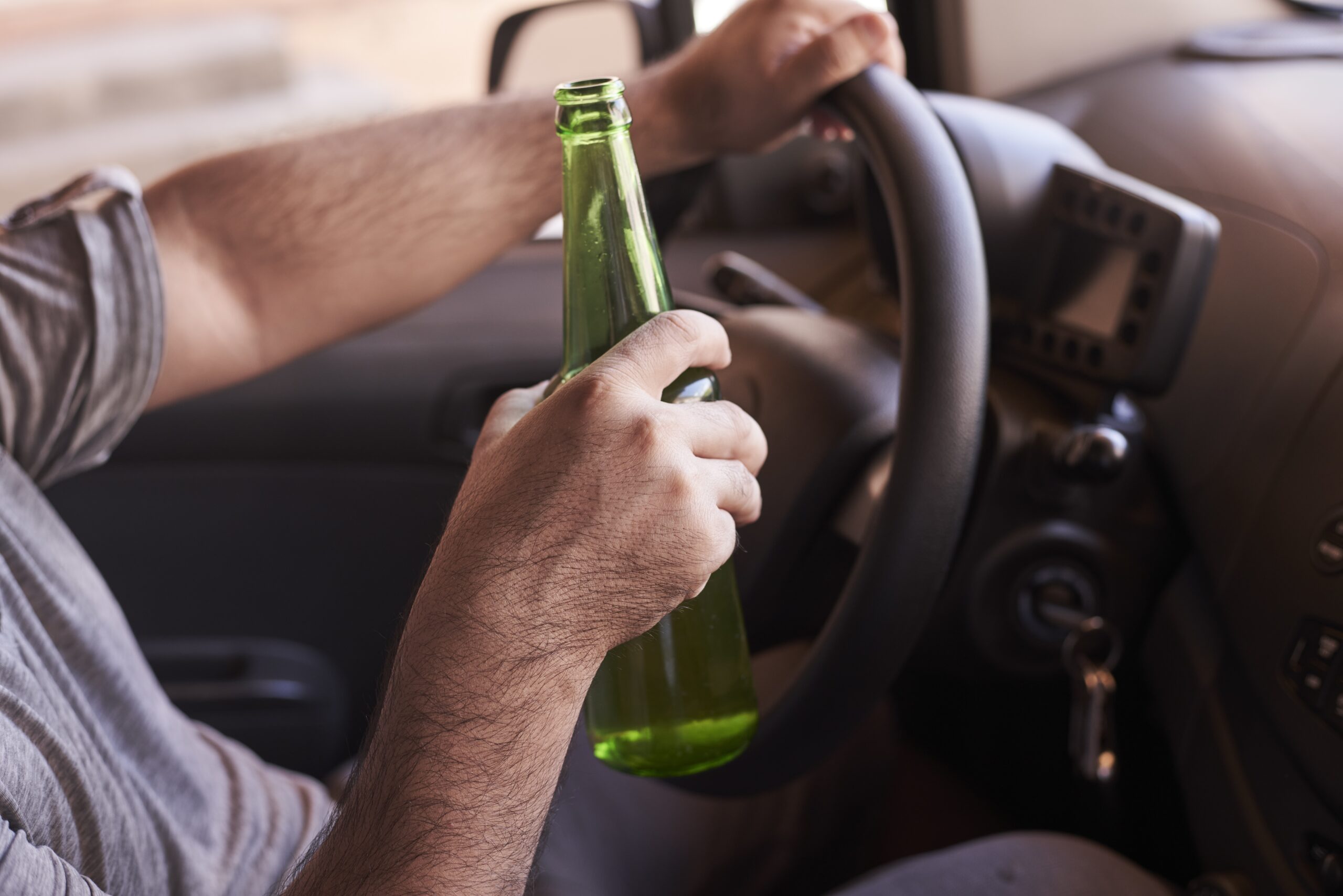 bottle of beer in a man s hands driving the car during daytime scaled
